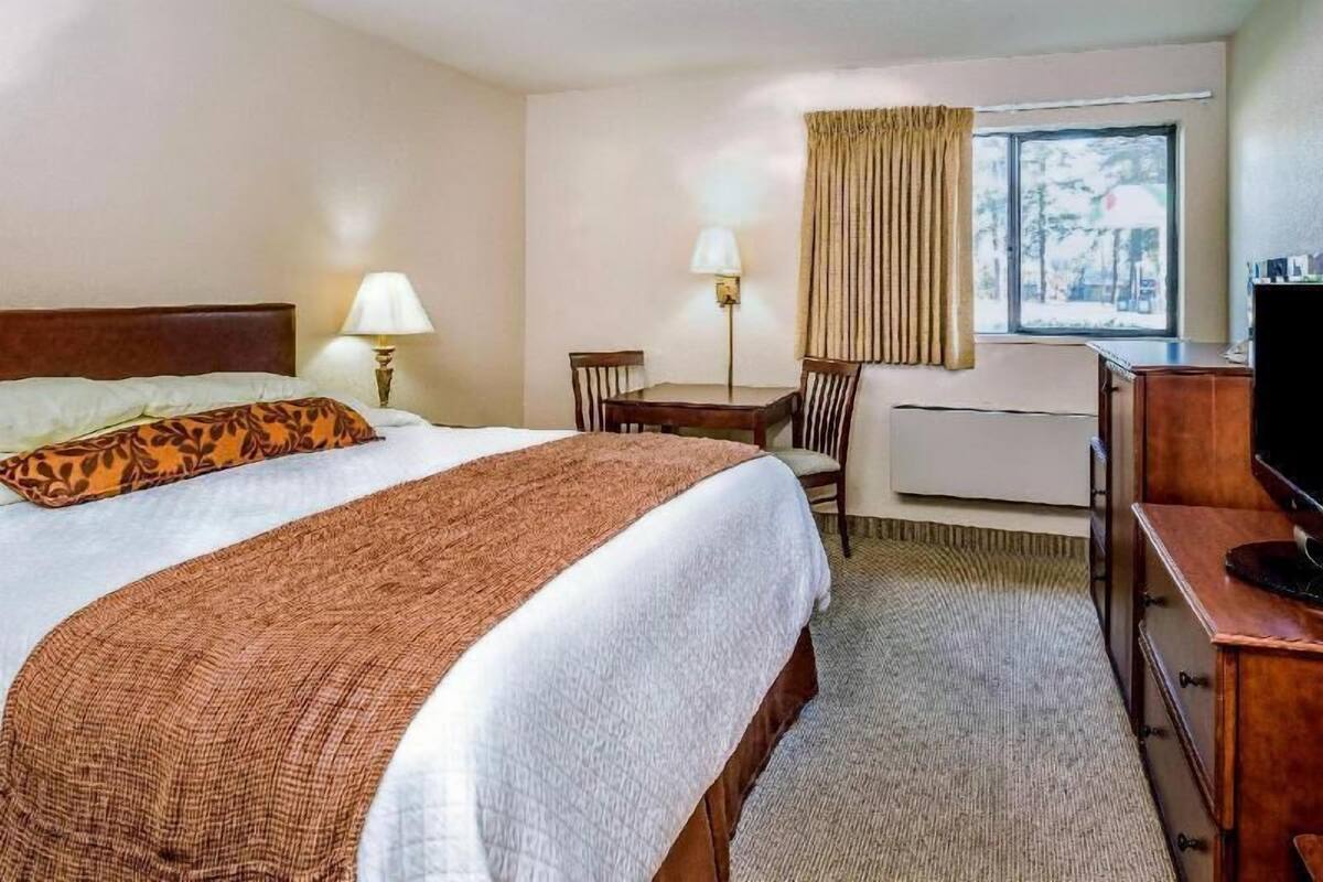 A hotel room with a bed, a desk, a chair, a TV, and a window with curtains.