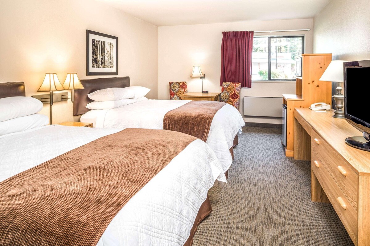 A hotel room with two beds, a desk, a television, and a window with curtains.