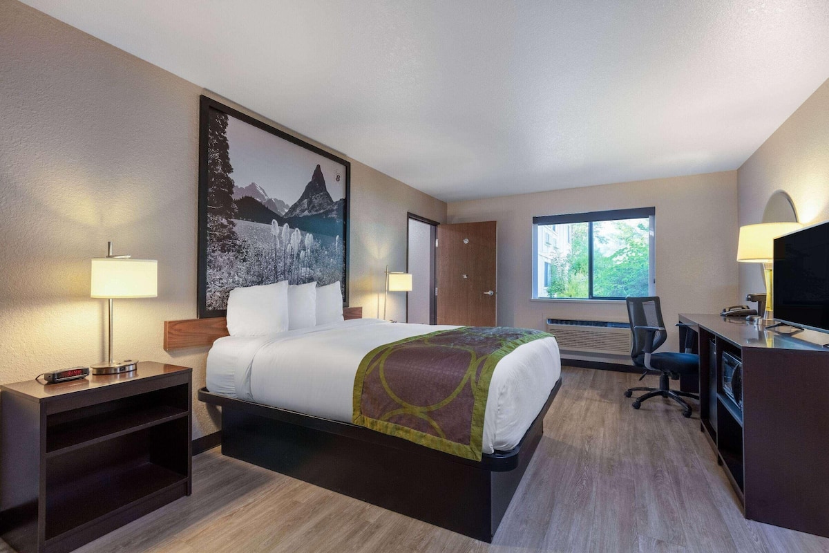 A hotel room with a bed, desk, chair, and a large window.