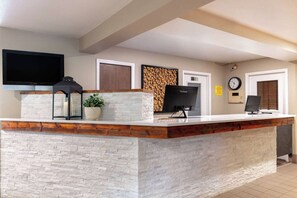 A reception desk with a stone facade, a flat-screen TV, a clock, and a firewood display. - Super 8 by Wyndham St. Regis (St. Regis)