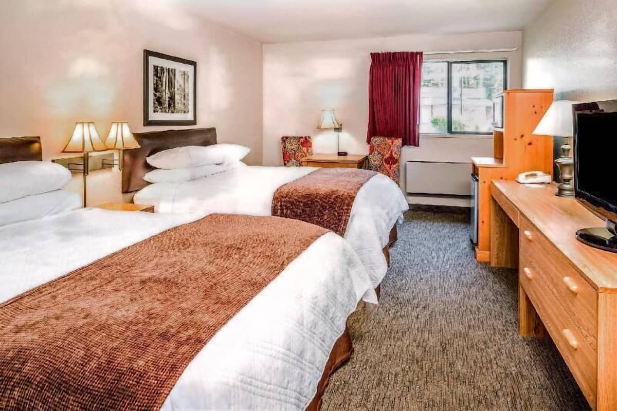 A hotel room with two beds, a desk, a TV, and a window with a view.