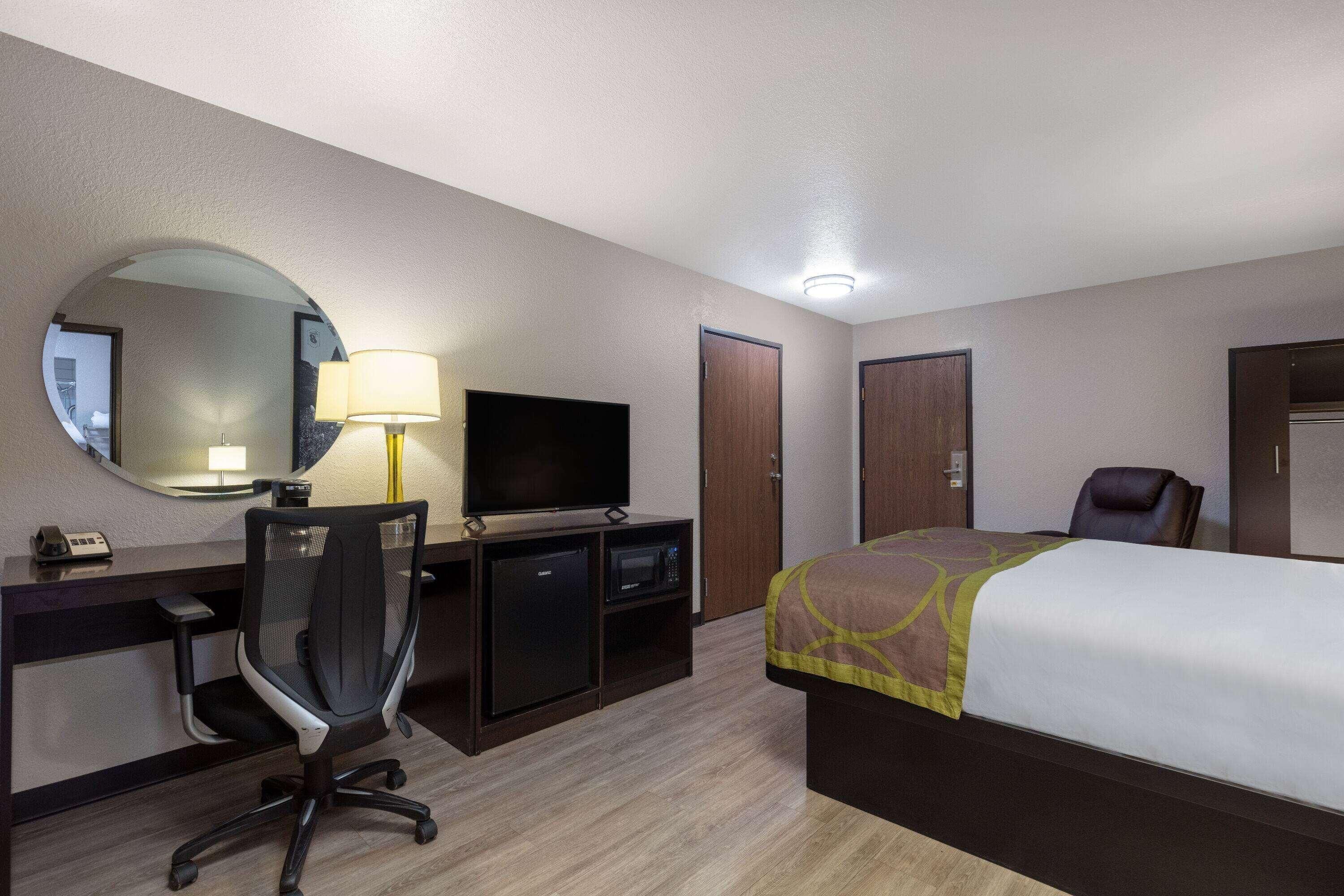 A hotel room with a bed, desk, chair, television, and a mirror.