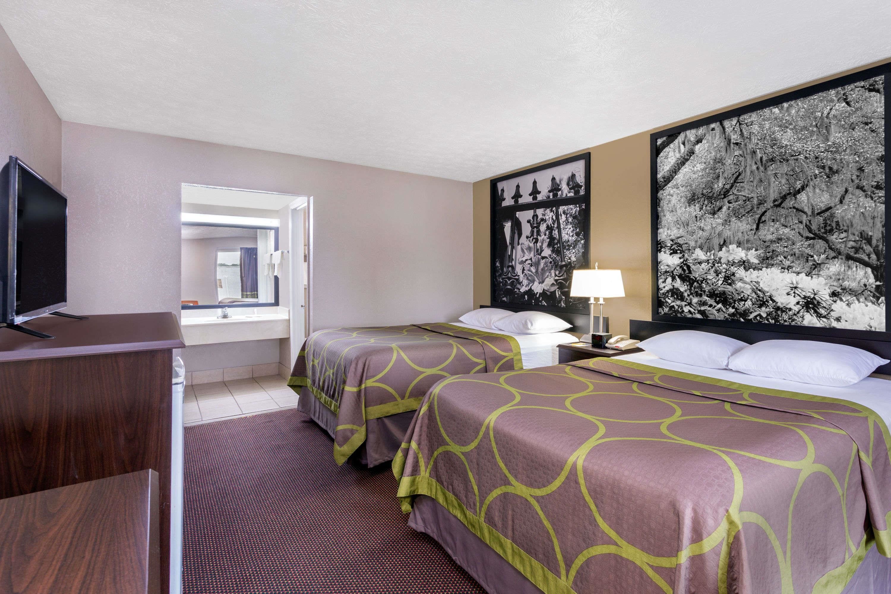 A hotel room with two beds, a desk with a TV, a window, and a large framed picture on the wall.
