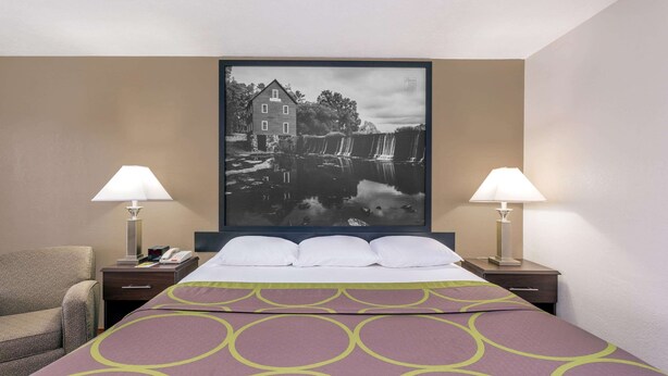 A hotel room with a bed, two bedside lamps, a chair, and a large framed picture on the wall. - Super 8 by Wyndham Locust Grove (Locust Grove)