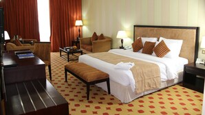 A hotel room with a large bed, a desk, a chair, a sofa, and a bench. - Grand Continental Hotel (Abu Dhabi)