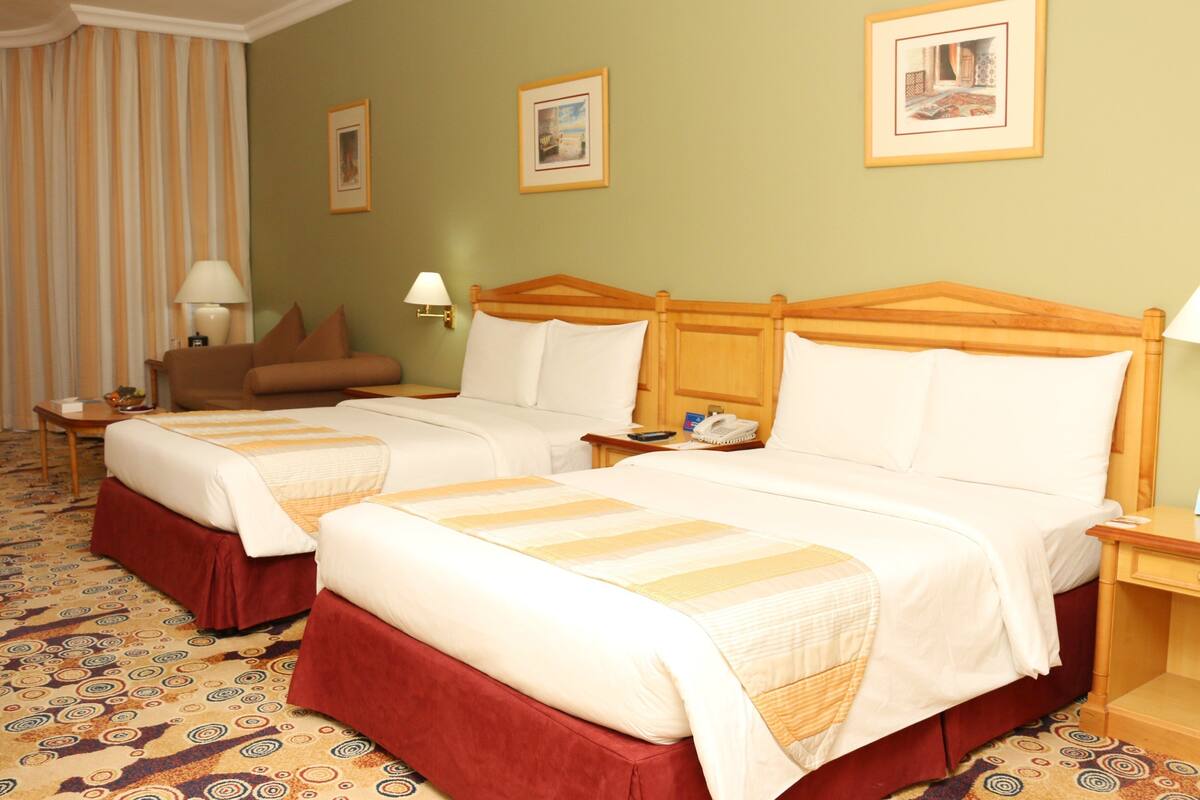 Une chambre d’hôtel avec deux lits, un canapé et une moquette à motifs.
