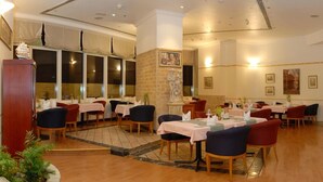 A restaurant with multiple tables, chairs, and a brick wall with a statue. - Grand Continental Hotel (Abu Dhabi)