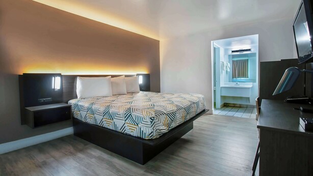 A modern bedroom with a bed, bedside tables, a TV, and a walk-in closet. - Motel 6 Tucson, AZ - East Williams Center (Tucson)