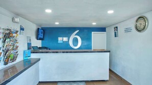 A reception desk with a large number '6' on the wall, a clock, and a sign stating 'Motel is not responsible for items left unattended.' - Motel 6 Tucson, AZ - East Williams Center (Tucson)