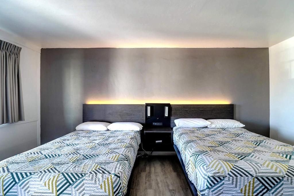 A hotel room with two single beds, a nightstand with a lamp, and a wall-mounted light fixture.