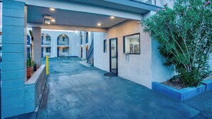 A modern building with a covered walkway, potted plants, and a staircase leading to an upper level. - Motel 6 Tucson, AZ - East Williams Center (Tucson)