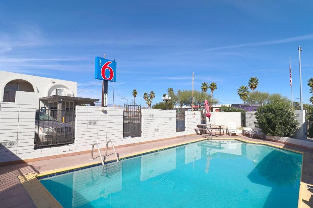 Una piscina con un cartel azul que indica el número de habitación 6, rodeada por un muro blanco con ventanas y una reja.