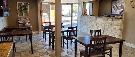 Un restaurante con pared de ladrillo, mesas y sillas de madera. Hay un mostrador con un menú y un letrero encima.