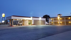 A gas station with a single-story building, a covered parking area, and a small adjacent structure with a balcony.