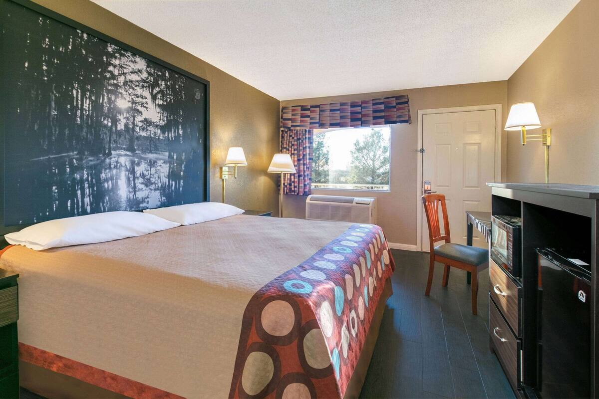 A hotel room with a bed, a desk with a chair, a refrigerator, and a window with curtains.