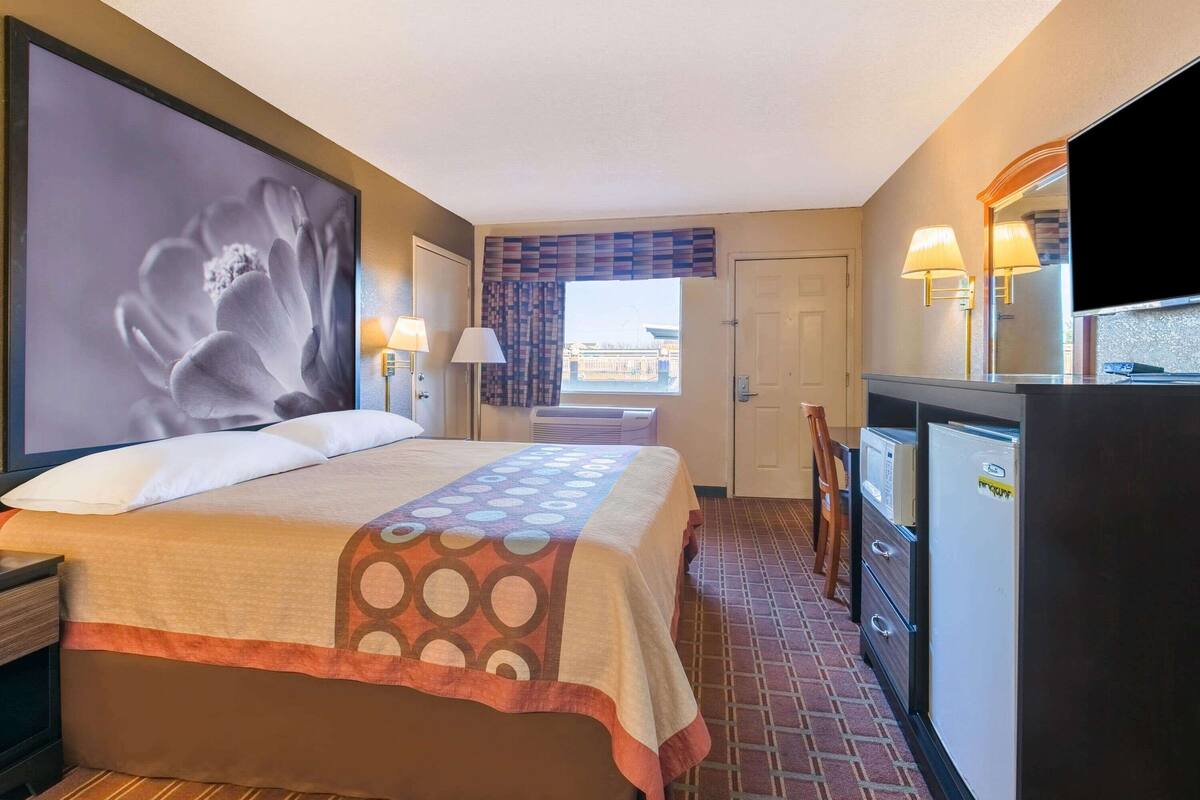 A hotel room with a large bed, a desk with a refrigerator, a TV, and a window with curtains.