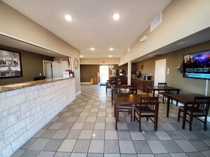 A hotel lobby with a reception desk, a clock, a TV screen, and a dining area with tables and chairs. - Super 8 by Wyndham Abilene North (Abilene)