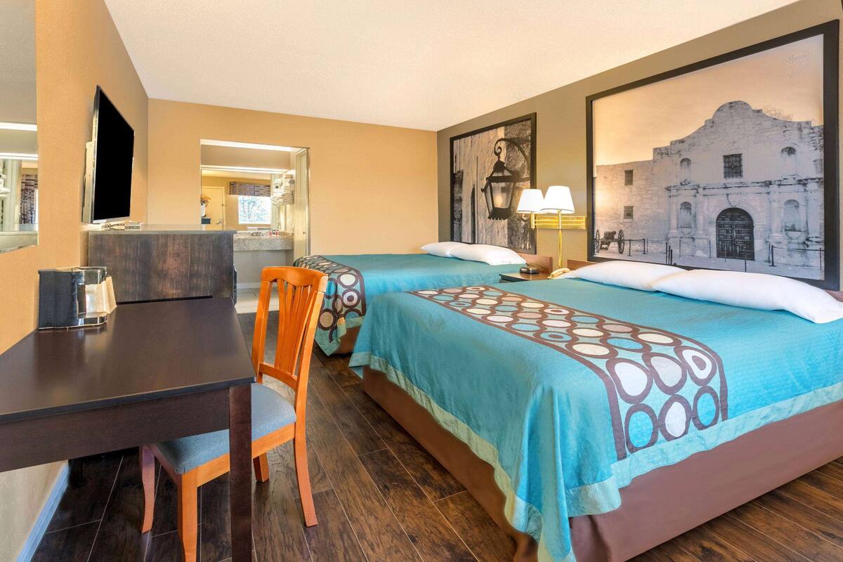 A hotel room with two beds, a desk, a chair, a TV, and artwork on the walls.