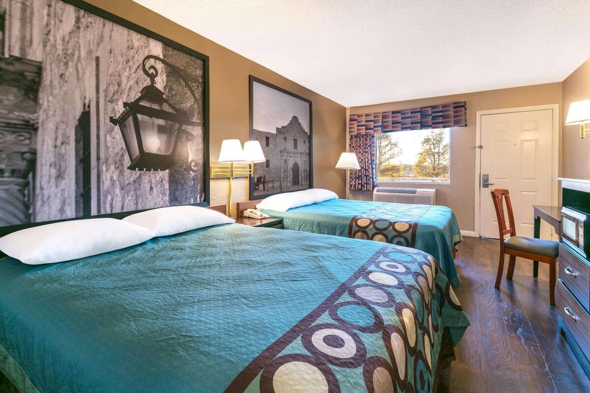 A hotel room with two beds, a desk with a chair, a window with a view, and a door.