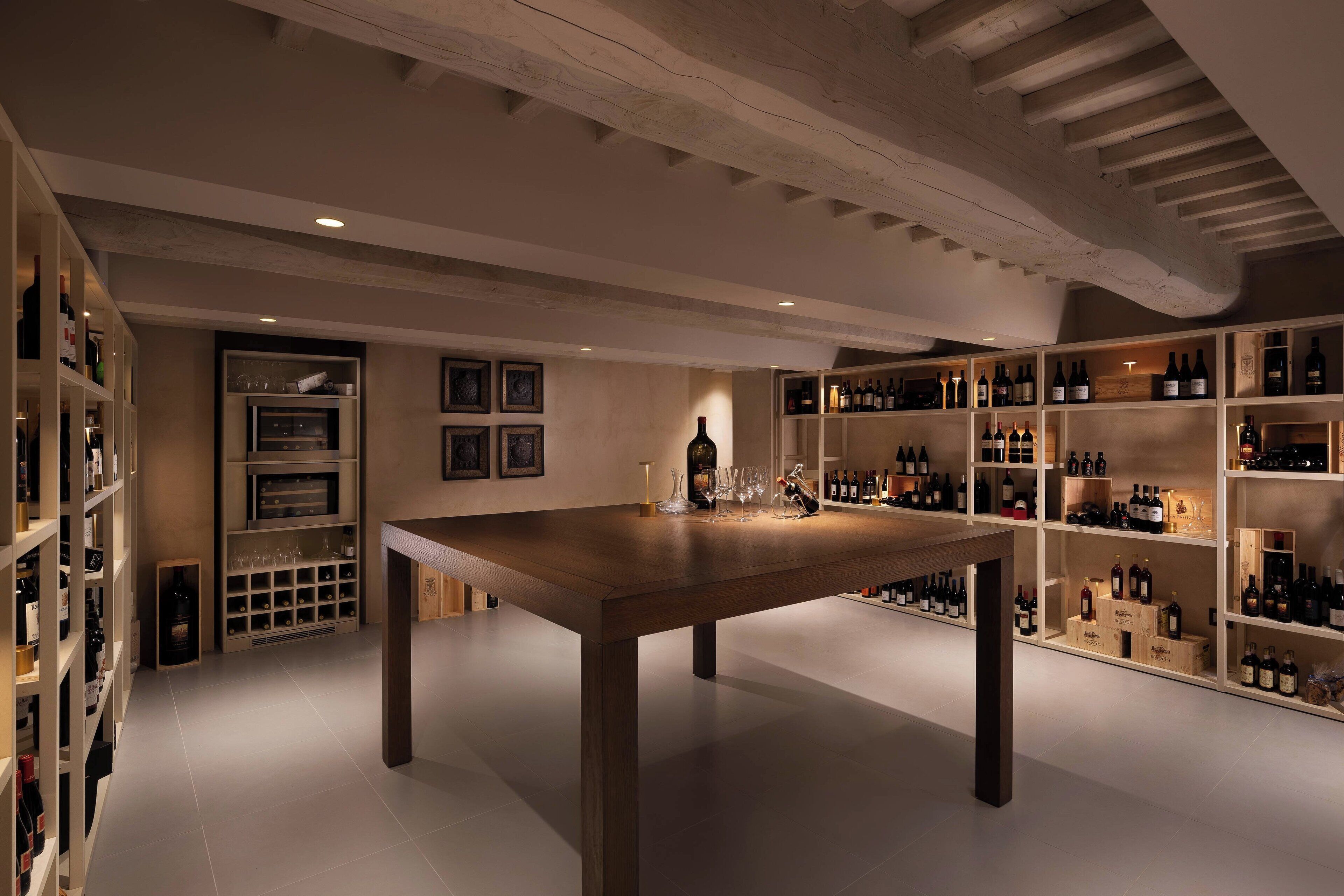 A wine cellar with wooden shelves, a central table, and wine bottles.
