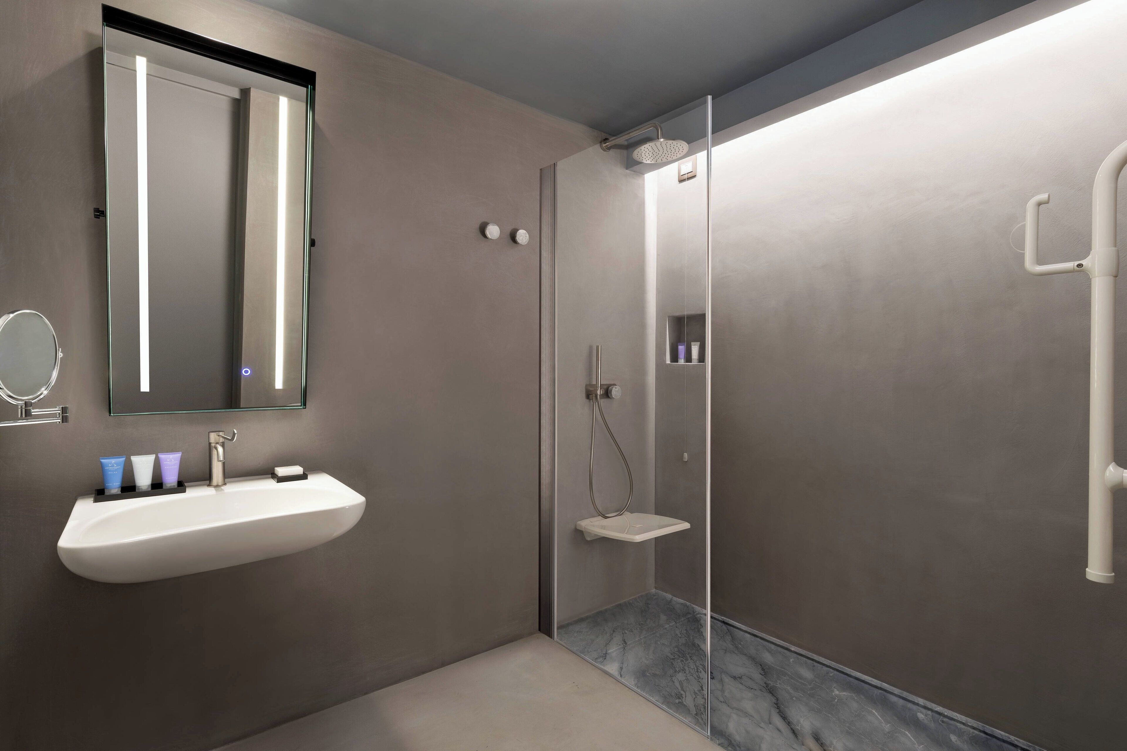 A modern bathroom with a large mirror, a sink with toiletries, and a glass-enclosed shower area.