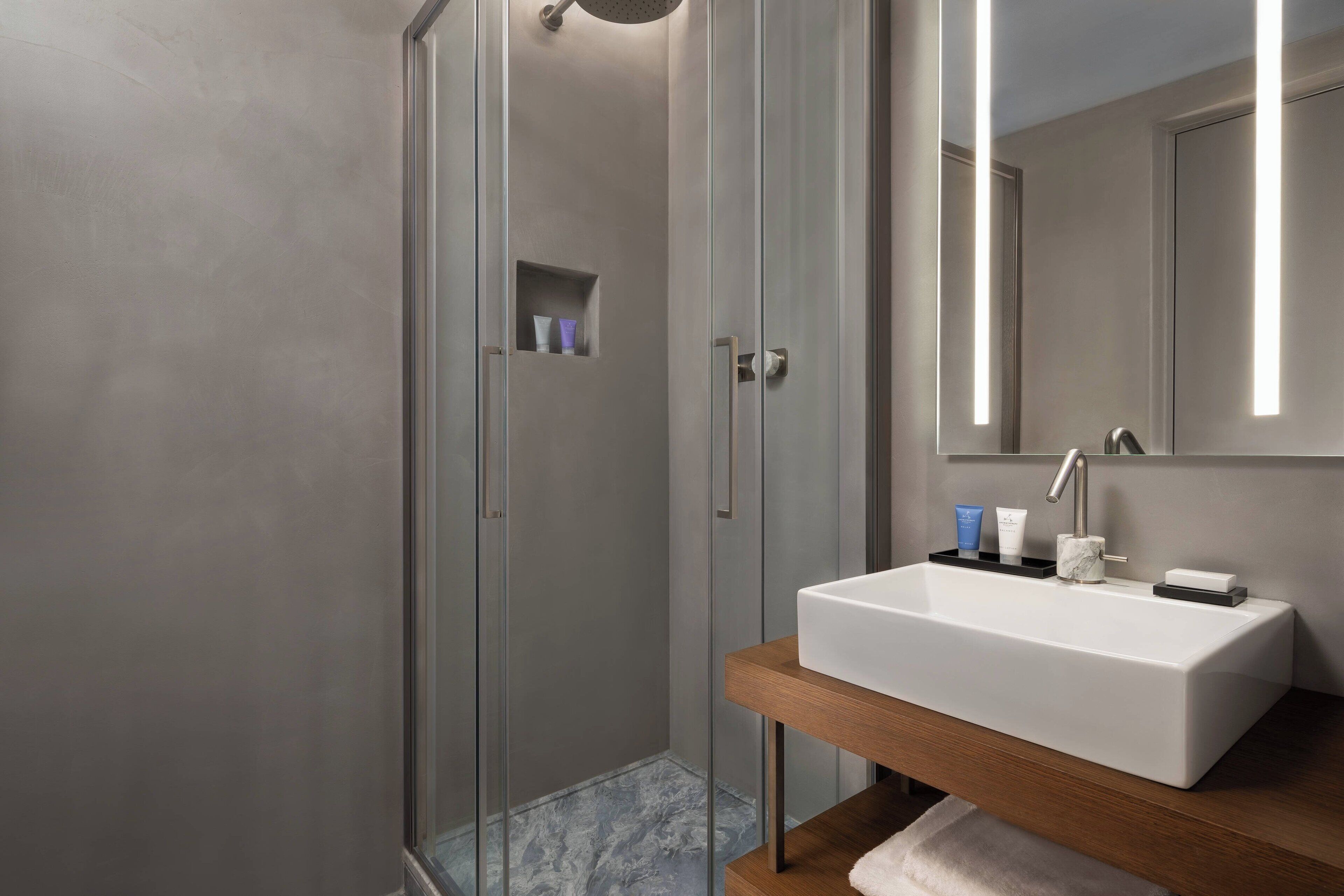 A modern bathroom with a glass-enclosed shower, a white sink, and a wooden vanity.