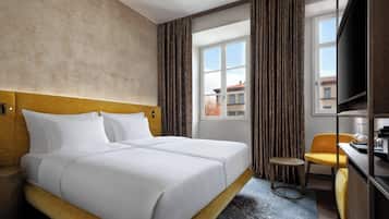 A hotel room with a double bed, a small round table, a chair, a television, and a window with curtains.