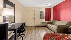 Quarto de hotel com escrivaninha, cadeira, sofá e colcha estampada.