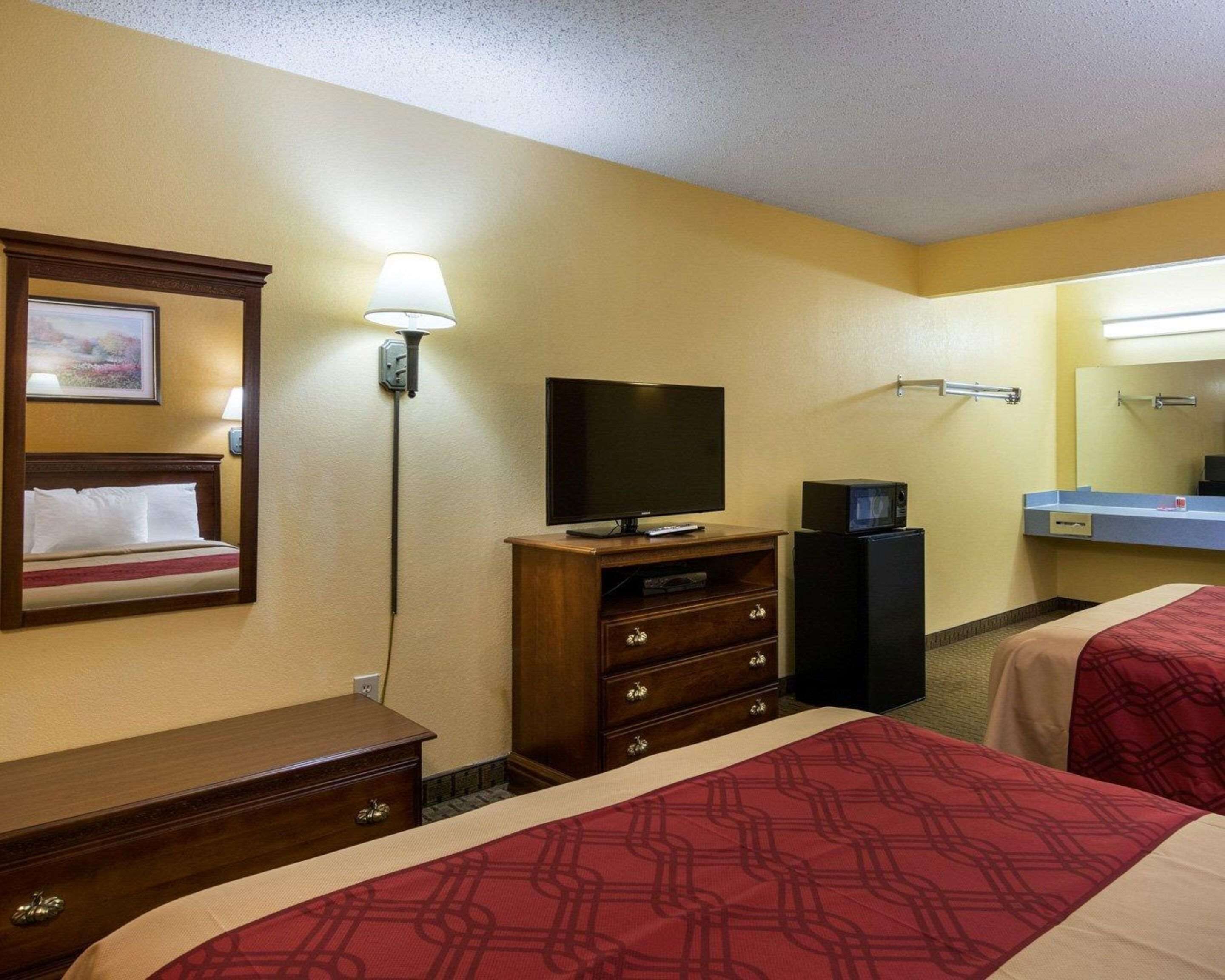 A hotel room with two beds, a television, a microwave, a dresser, a lamp, and a framed picture on the wall.
