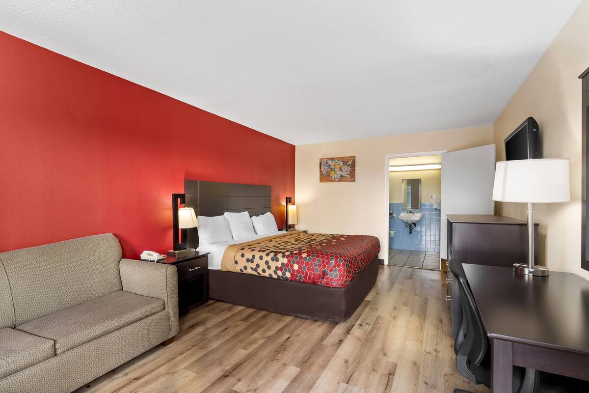 Habitación de hotel con cama, sofá, escritorio y baño visible a través de una puerta abierta.