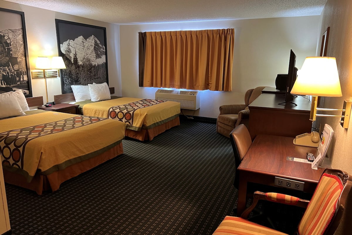 Une chambre d’hôtel avec deux lits, un bureau, une chaise, une télévision, une lampe et un tableau au mur.