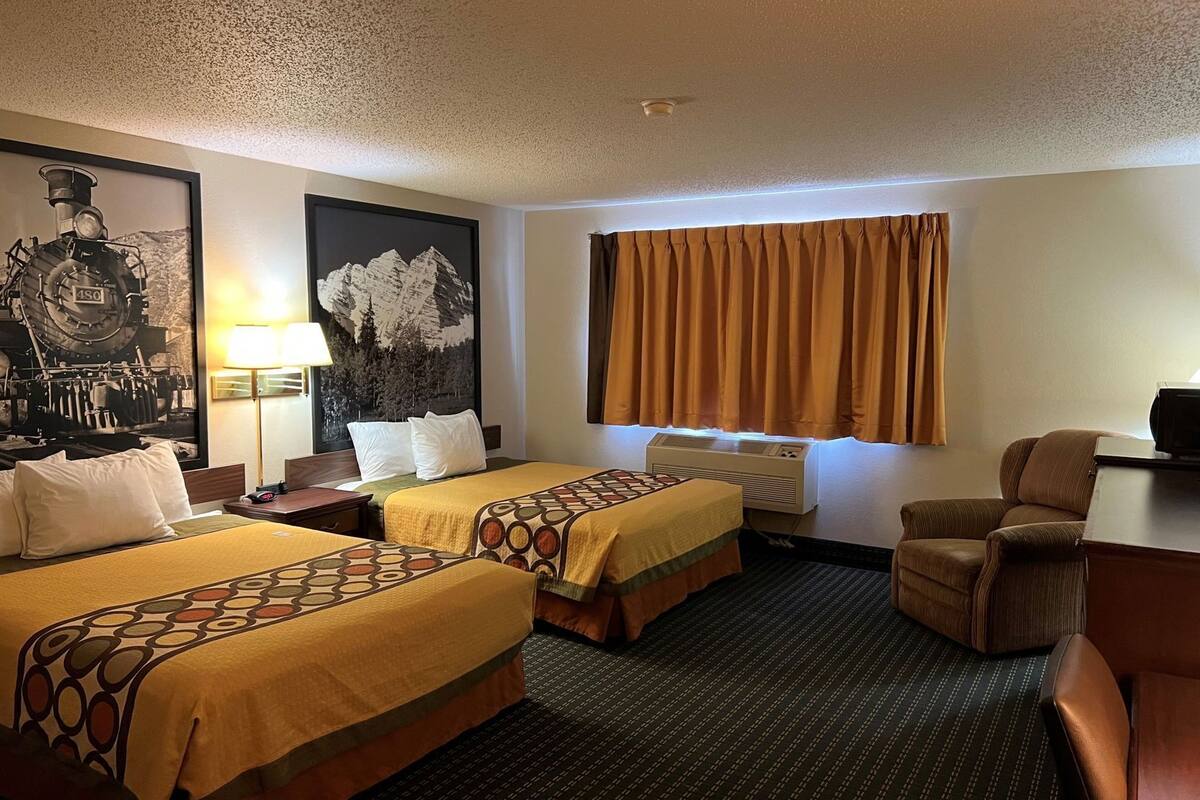 Une chambre d’hôtel avec deux lits, un bureau, une chaise, une lampe, un radiateur et un grand tableau encadré au mur.