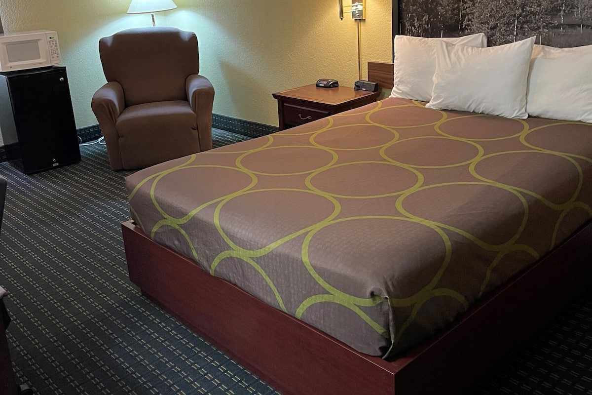 Une chambre d’hôtel avec un grand lit, une chaise, un bureau avec une lampe et un téléviseur fixé au mur.