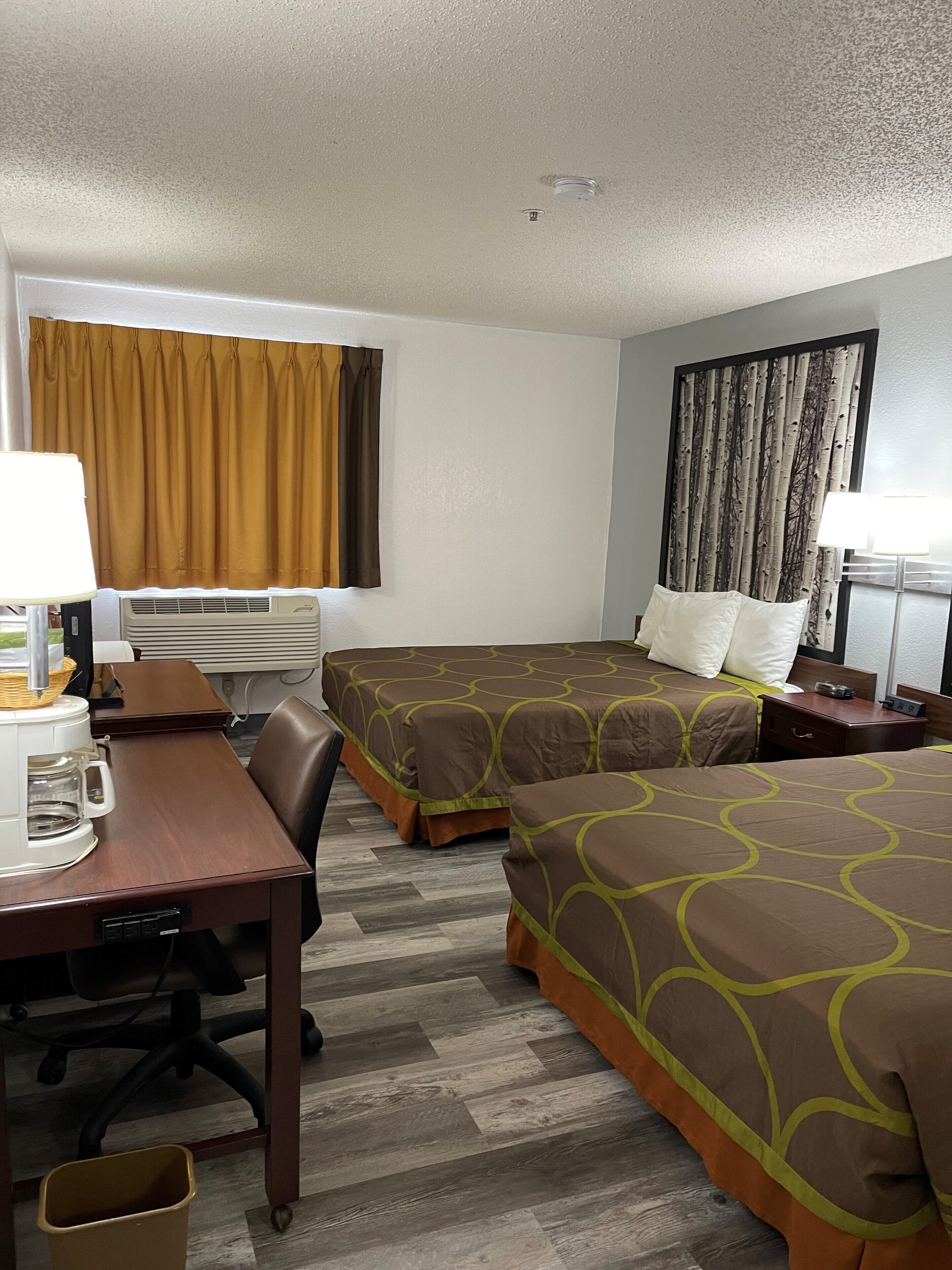 Habitación de hotel con dos camas, un escritorio con cafetera, una silla y una ventana con cortinas.