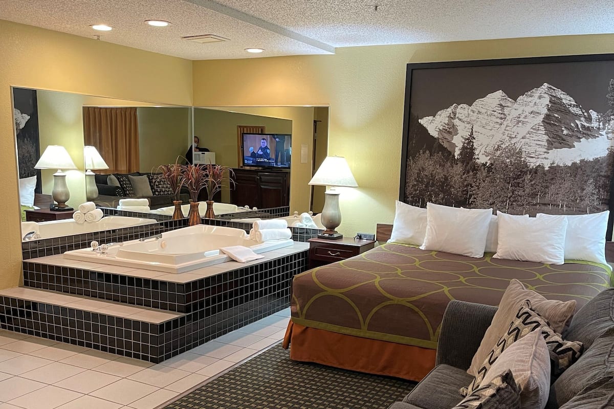 Une chambre d’hôtel comprenant un lit, un canapé, une télévision, une salle de bain avec baignoire et un grand miroir.