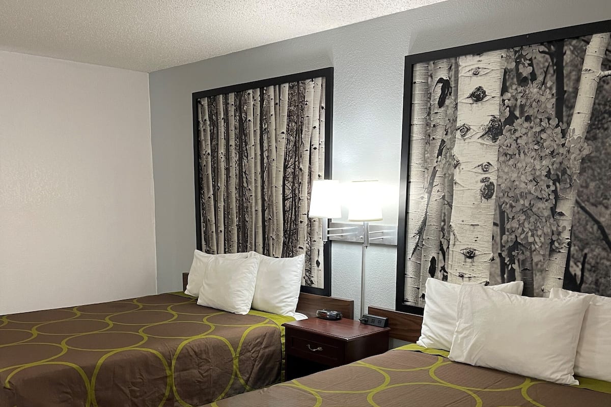 Une chambre d’hôtel avec deux lits, une table de chevet, une lampe et un mur décoré d’un rideau sur le thème de la nature.