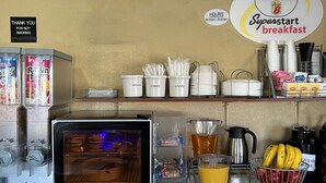 Un espace réservé au petit-déjeuner, équipé d’un réfrigérateur rempli de nourriture, d’une machine à café et d’un panneau indiquant les heures de service du petit-déjeuner Superstart.