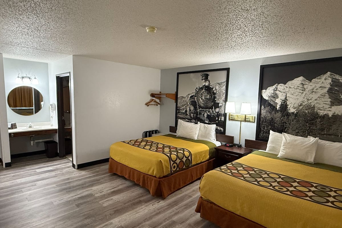 Une chambre d’hôtel avec deux lits, un bureau, une chaise, un miroir et un grand tableau mural.