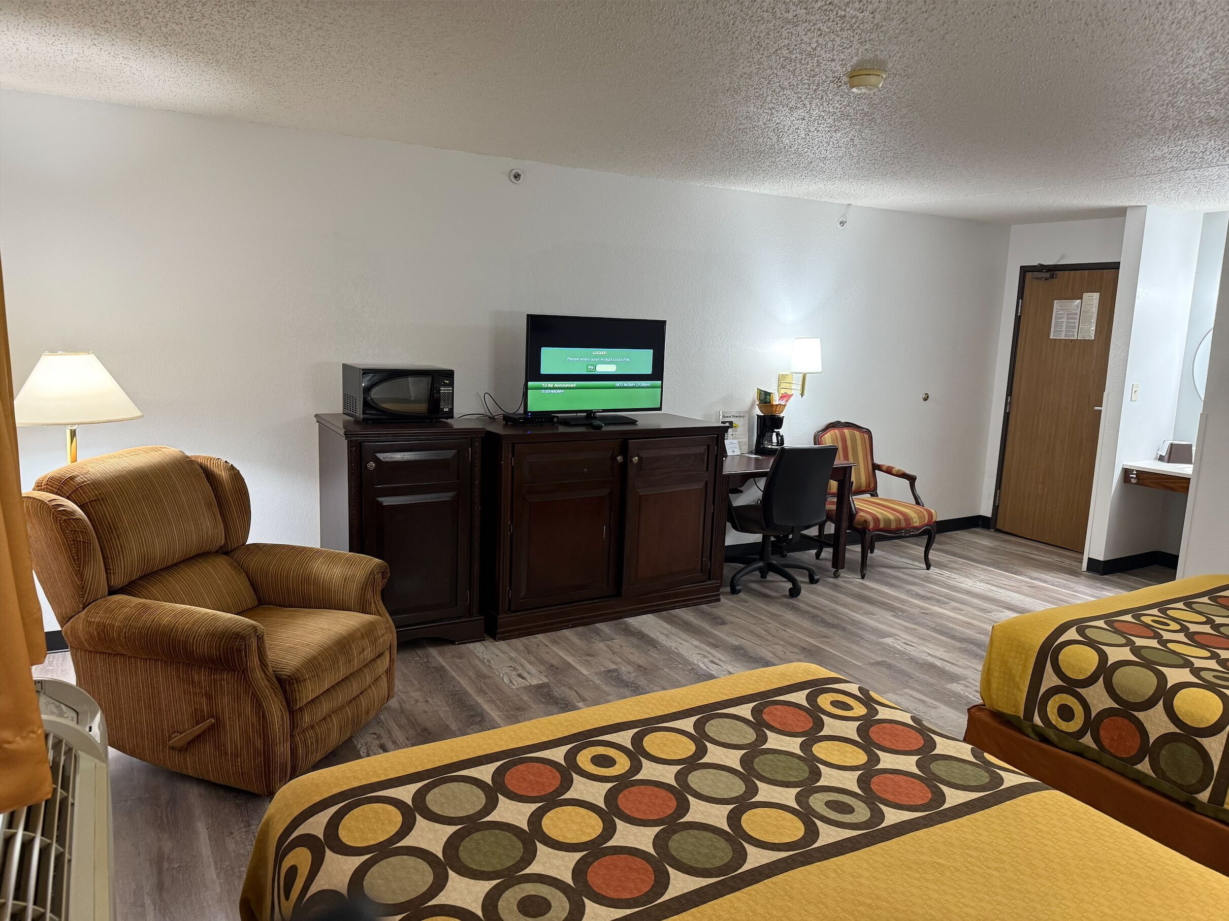 A hotel room with two beds, a desk with a computer, a chair, a lamp, and a microwave.