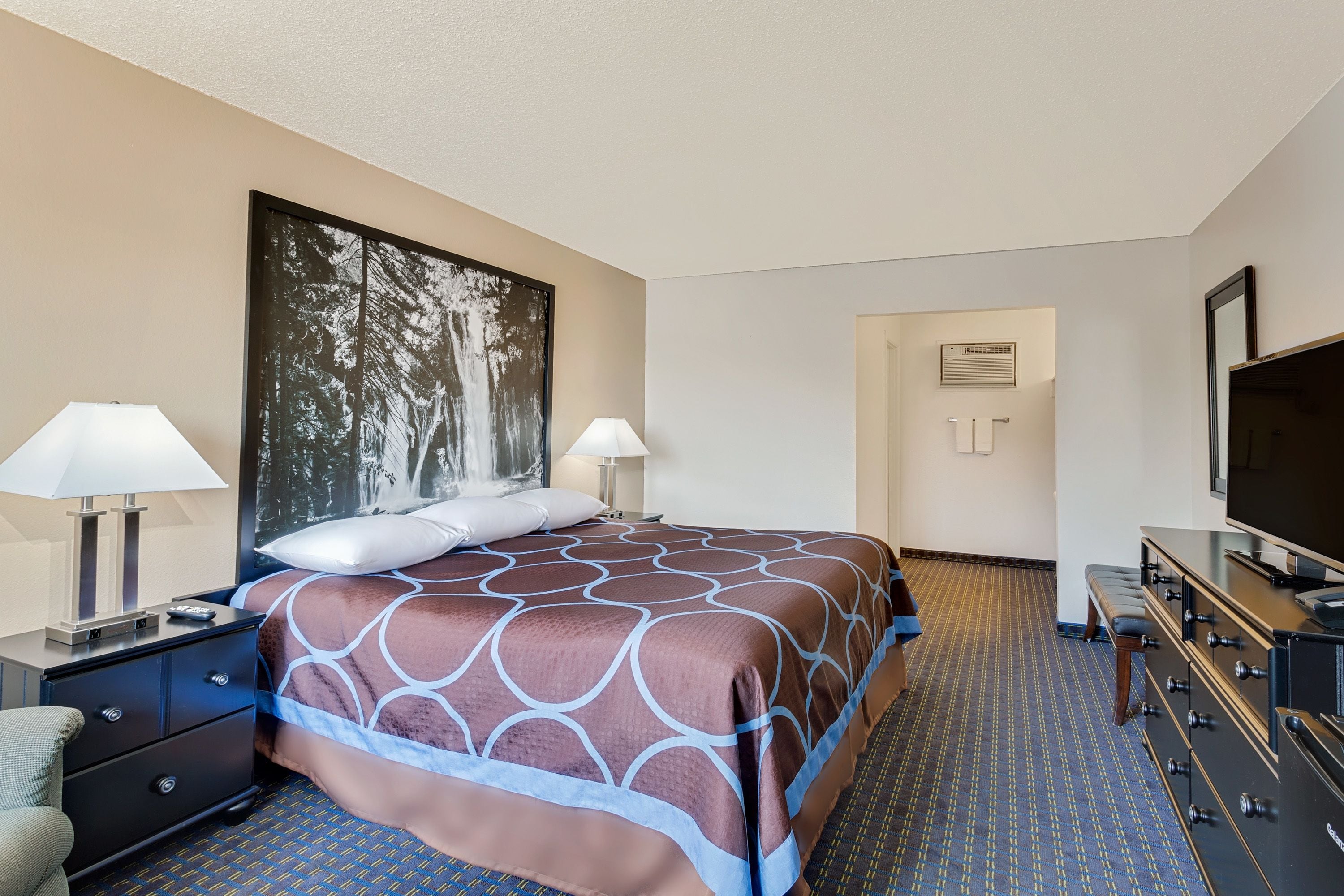 A hotel room with a large bed, two bedside tables with lamps, a television, and a door leading to a bathroom.