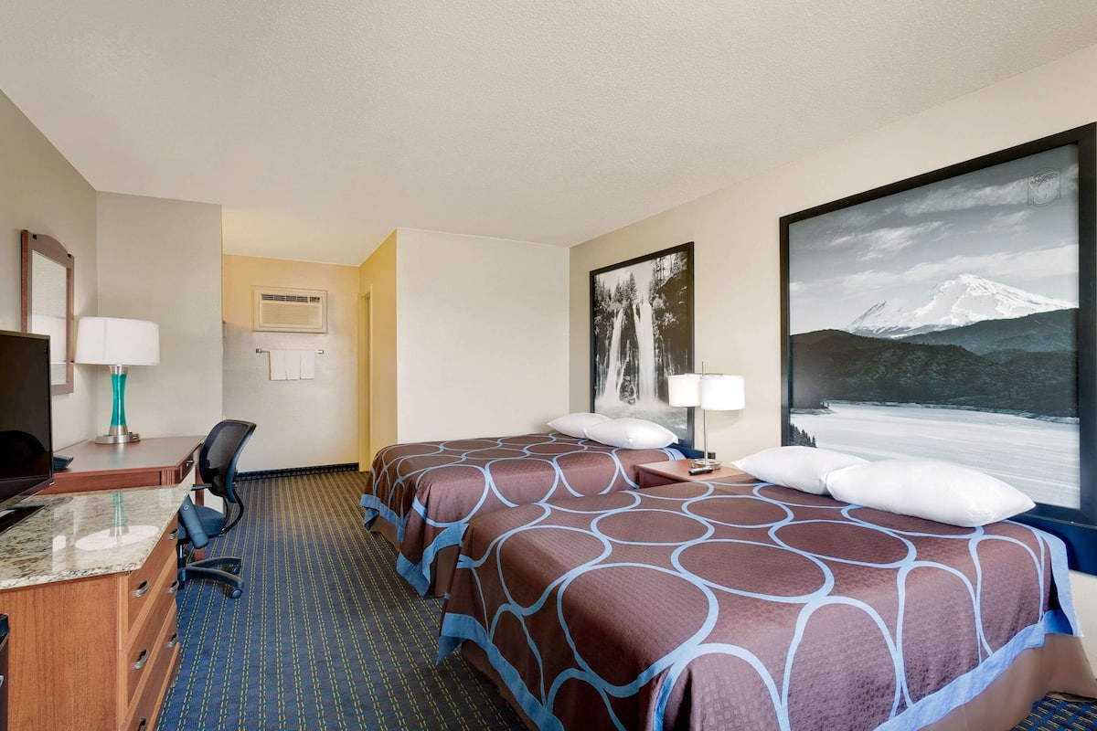 A hotel room with two beds, a desk with a computer, a chair, a TV, and a large window with a mountain view.