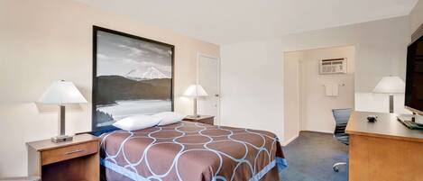 Une chambre d’hôtel comprenant un lit, deux tables de chevet avec des lampes, un bureau avec un ordinateur et une grande fenêtre donnant sur la montagne.