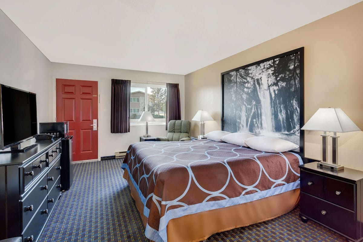 A hotel room with a bed, a TV, a dresser, a chair, and a window with curtains.