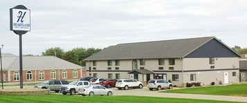 Hotel and Suites Heartland con un estacionamiento lleno de coches, un edificio de ladrillo y una estructura grande con techo plano.