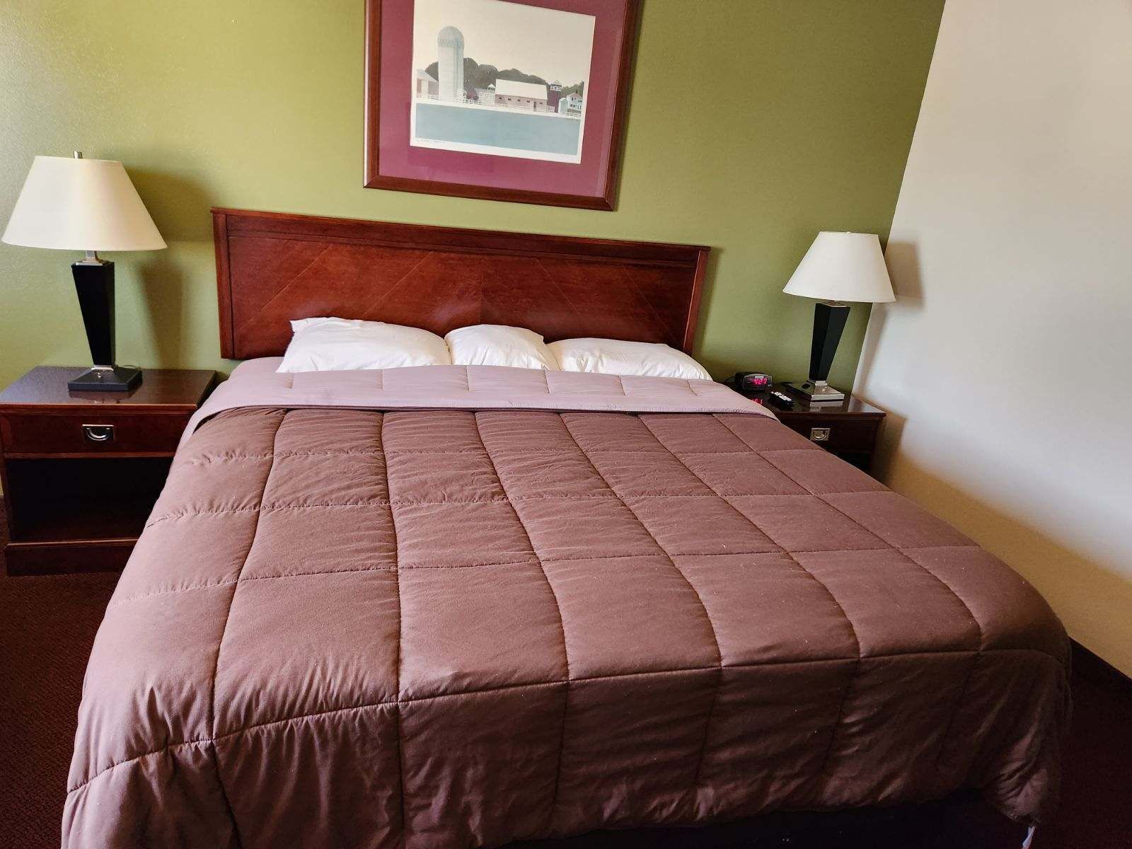 A neatly made bed with a brown quilt, two bedside tables with lamps, and a framed picture on the wall.