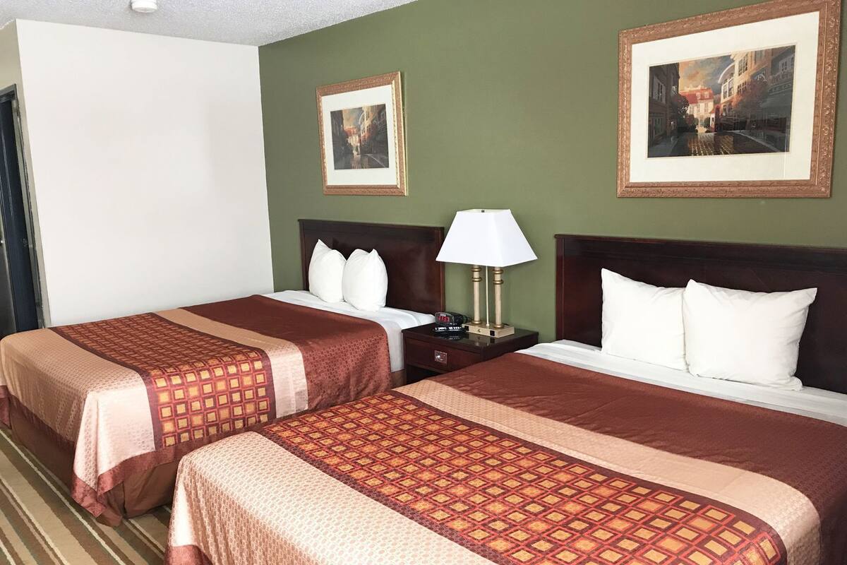 A hotel room with two beds, a nightstand, a lamp, and two framed pictures on the walls.