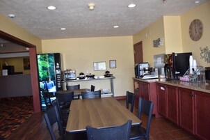 Un restaurante con una mesa y sillas de madera, una zona de cocina con electrodomésticos y un reloj en la pared.