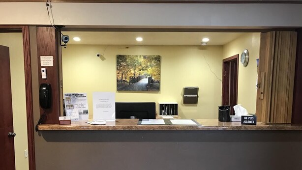 A reception area with a counter, a painting of a bridge, a clock, and a 'No Pets Allowed' sign. - Heartland Hotel and Suites (Rock Valley)