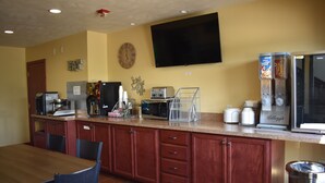 A kitchen with wooden cabinets, a microwave, toaster, coffee maker, and a trash can. - Heartland Hotel and Suites (Rock Valley)