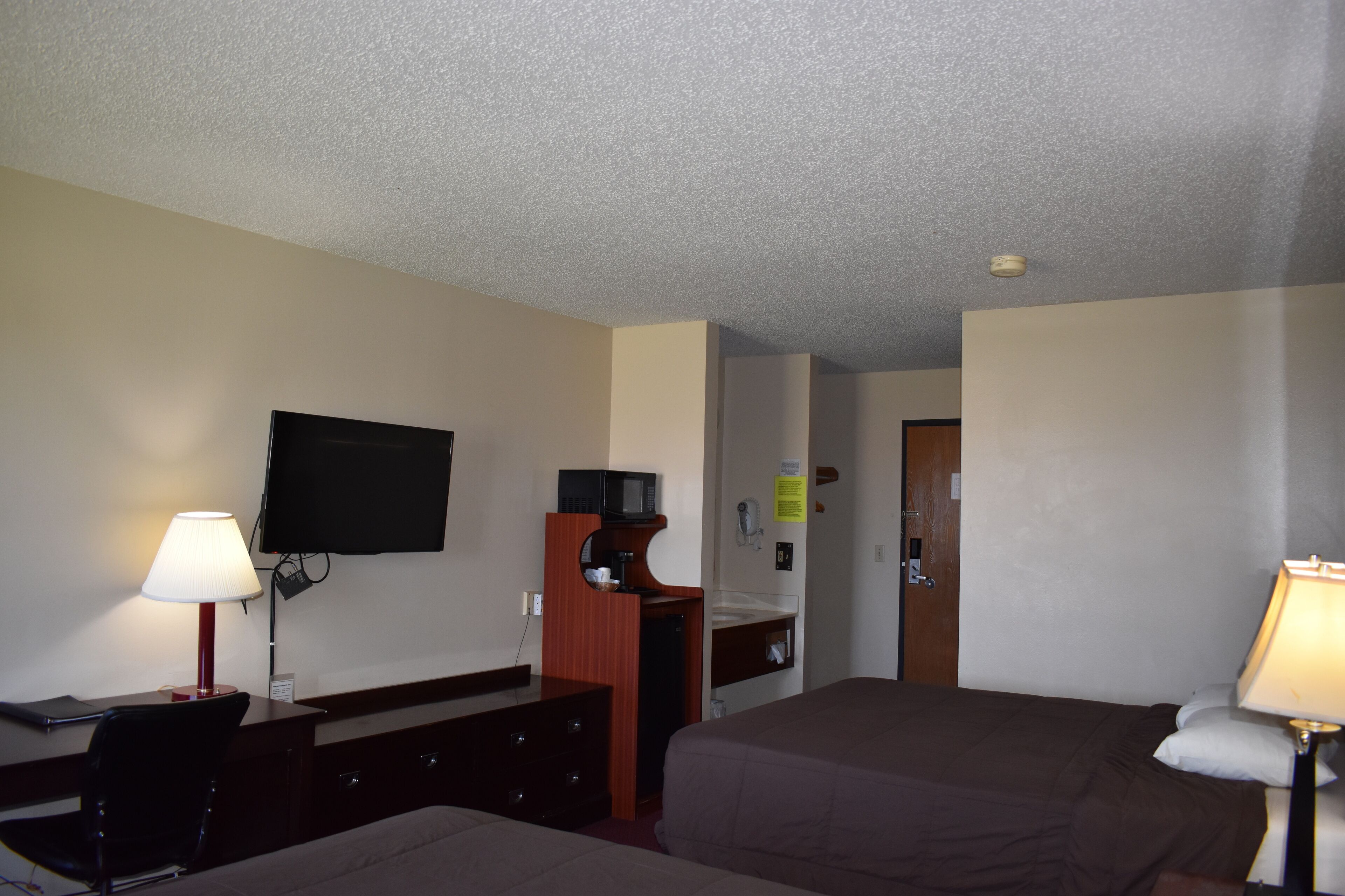 A hotel room with two beds, a desk with a chair, a television mounted on the wall, and a bathroom visible through an open door.